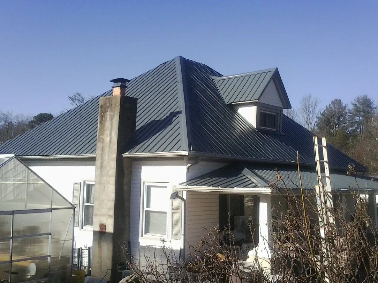 Dark blue standing seam metal roof on a white farmhouse with dormer — Slate & Tile Roof Repair by Roofing Brothers in Watchung