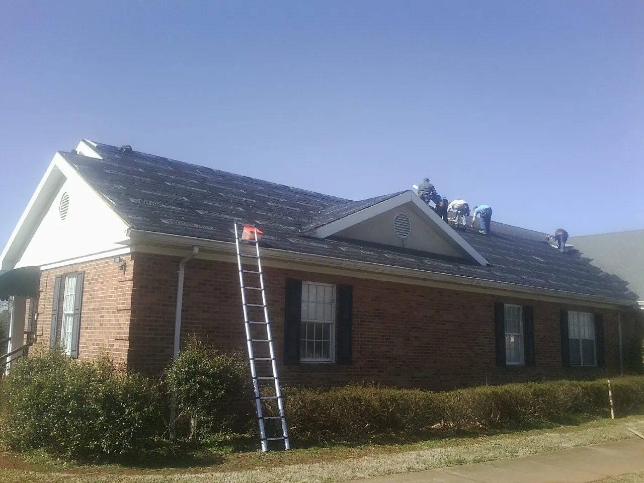 Crew tearing shingles off a brick ranch roof with a ladder set — Emergency Roof Repair work by our crew in Watchung