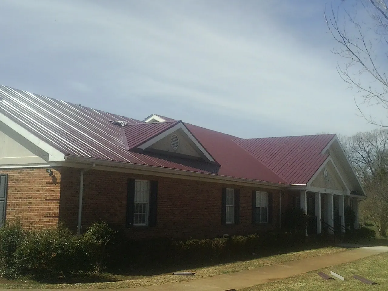 Red metal roof with gabled entries on a long brick building, from a Hail Damage Roof Repair job in Watchung