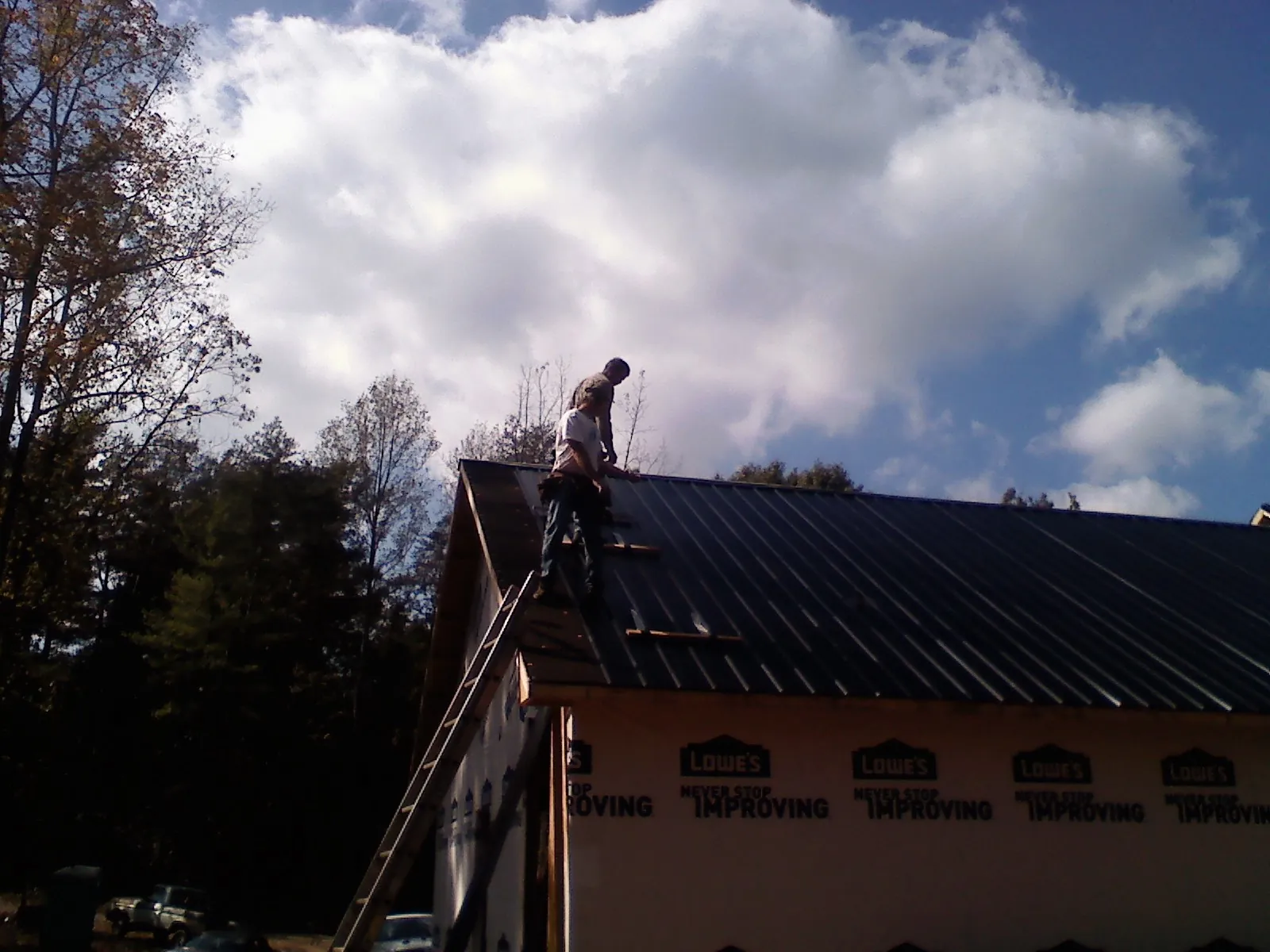 Roofer fastening dark metal panels high against a cloudy sky, from a Roof Inspection job in Watchung