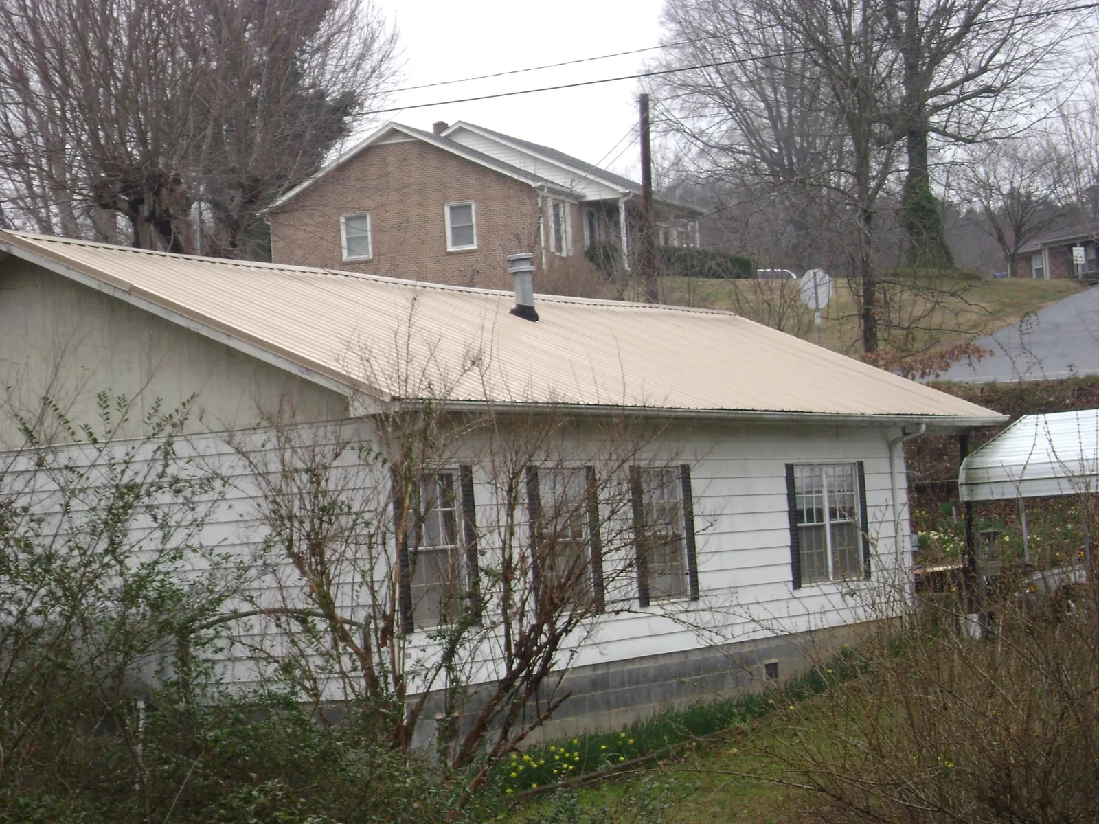 Tan metal roof on a white sided house set into a hillside — Commercial Roofing by Roofing Brothers in Watchung